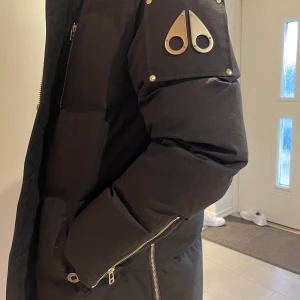 Svart dunjacka med pälsdetaljer storlek M - Säljer en snygg svart dunjacka från Moose Knuckles. Jackan har en fluffig pälsdetalj på huvan och coola metalliska detaljer på ärmarna. Perfekt för kalla vinterdagar med sin varma och vadderade design. Dragkedjorna ger en extra touch av stil. Passar perfekt för både vardag och fest! ny pris 11900 kr på therlunds. Mitt pris 7500 kr. Köpt i januari 2024 använd 1 månad. Helt i nyskick! 