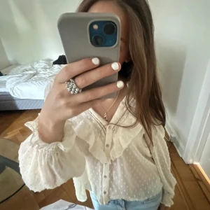 Vit blus med volangdetaljer - Säljer en superfin vit blus med volangdetaljer och knappar framtill. Blusen har långa ärmar och ett diskret prickigt mönster. Perfekt för både vardag och fest! den är i s men sitter som xs🕊️🩷