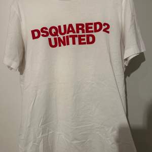 Säljer en snygg vit t-shirt från Dsquared2 med röd text 'DSQUARED2 UNITED' på bröstet. Perfekt för en casual look och passar till alla tillfällen. Tillverkad i Italien, vilket ger den en lyxig känsla. Skön och stilren design! Nypris 1700kr köpt på johnells. Väldigt stor i storlek, skulle säga att den är i storlek m/L normalt sätt.