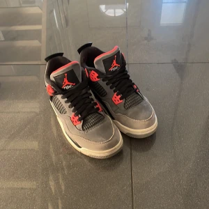 Grå och svarta Nike Air Jordans 4 - Nike Air Jordans 4 Infrared. Grått och svart med  röda detaljer. Skorna är i mycket bra skick och har en snygg design med snörning och en bekväm passform. Perfekta för både vardag och fest! Köptes för ungefär 3200kr. Priset kan diskuteras!!!! Kommer i samma låda som den köptes i. Kan visa verifierad autenticitet!