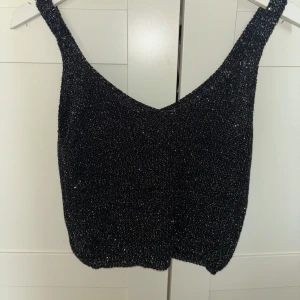 Svart glittrig linne - Snygg svart glittrig linne perfekt för festliga tillfällen. Den har en djup v-ringning och är ärmlös, vilket gör den idealisk för en utekväll. Materialet är stretchigt och bekvämt. Köpt på marknad utomlands och är helt oanvänt🩷🩷