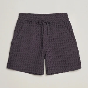 Nearly Black Porto Waffle Shorts från OAS - Säljer ett par snygga svarta Porto Waffle shorts från OAS i storlek M. De har en cool textur och är perfekta för en avslappnad stil. Shortsen har en bekväm passform med dragsko i midjan och praktiska fickor. Perfekta för sommardagar eller en chill dag hemma.
