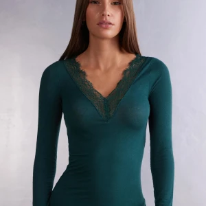 Grön långärmad topp med spetsdetaljer - Snygg grön långärmad topp med v-ringning och spetsdetaljer. Perfekt för både vardag och fest. Toppen har en tight passform men är samtidigt stretchig så läger sig perfekt efter just din kroppsform! Superfin att matcha med jeans eller kjol! Xs/s
