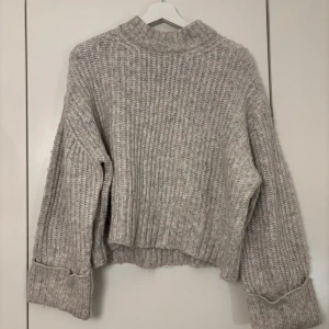 Grå stickad tröja från Gina Tricot - Mysig grå stickad tröja från Gina Tricot i storlek S. Perfekt för kyliga dagar med sin croppade design och långa ärmar. Tröjan har en ribbad struktur som ger en stilren look. Passar både till vardags och mysiga hemmakvällar.
