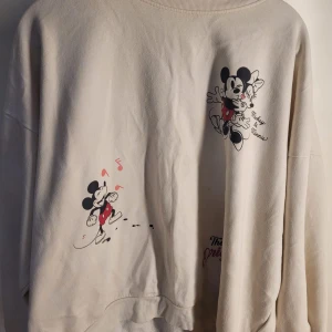 Beige Disney-tröja med Musse Pigg-motiv - Säljer en superfin beige tröja från Disney med Musse Pigg-tryck. Tröjan är i bra skick och har långa ärmar. Perfekt för alla Disney-fans som vill ha något mysigt och stilrent i garderoben. Passar perfekt till höst och vår!