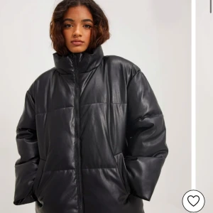Svart pufferjacka - Säljer en snygg svart pufferjacka i skinnmaterial Jackan har en hög krage och dragkedja framtill, perfekt för kalla dagar. Den är oversized och har långa ärmar, vilket gör den superbekväm och trendig. Perfekt för höst och vinter!