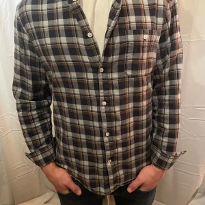 Rutig skjorta från NN07 - Säljer en snygg rutig skjorta från NN07 i mörka toner av svart, grått och brunt. Funkar både till vardags och lite finare tillfällen. 