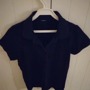 Svart kortärmad pikétröja, Strlk: Small / 34-36. - Säljer en stilren svart kortärmad pikétröja. Lämplig till vardags. Tröjan har en klassisk krage och knappar framtill. Den är i använt men ok skick - se bilder för egen bedömning. Inga hål eller liknande.