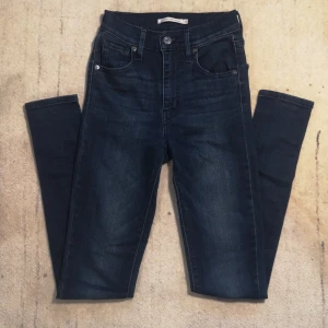 Mörkblå jeans från Levi's - Säljer ett par mörkblå Levi's Mile High Super Skinny jeans i storlek 23. De är högmidjade och har en tight passform som sitter perfekt. Klassisk femficksdesign med knapp och dragkedja framtill. Perfekta för både vardag och fest!