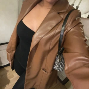 Brun skinnjacka - Säljer en snygg brun skinnjacka i mycket bra skick. Den har en klassisk kavajstil med knappar framtill och en normal passform. Perfekt för höst och vår, och funkar lika bra till vardags som till fest. Jackan har långa ärmar och en stilren design som gör den lätt att matcha med olika outfits.