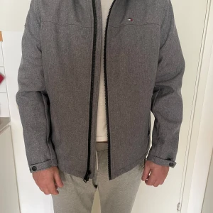 Grå jacka från Tommy Hilfiger - Säljer en snygg grå jacka från Tommy Hilfiger i mycket bra skick. Jackan har en dragkedja framtill och är fodrad med mjuk fleece för extra värme. Perfekt för höst och vår! Den har långa ärmar och en stilren design som passar till det mesta. 🧥