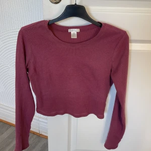 Vinröd ribbad croppad tröja från fashionnova  - Säljer en snygg vinröd ribbad tröja från Fashionnova. Den är croppad och har långa ärmar, perfekt för höst och vår. Tröjan är i bra skick och passar både till vardags och fest. Superfin att matcha med höga jeans eller kjol!