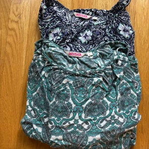 Mönstrade blusar från Indiska - Två vackra blusar från Indiska i olika mönster. Den ena är grön och vit med ett intrikat paisleymönster, och den andra är mörkblå med blommönster i ljusa toner. Båda har långa ärmar och en lös passform, perfekta för vår och sommar. 40kr/st eller 60 för båda