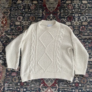 Vit stickad tröja från ASOS  - Mysig vit stickad tröja från ASOS DESIGN i storlek 34. Den har ett snyggt flätmönster på framsidan och ribbade kanter vid hals, ärmslut och nederkant. Perfekt för kalla dagar när du vill vara både varm och stilren. 🧶✨I bra skick, lite nopprig. 