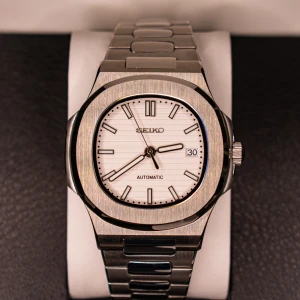 Seiko Mod  - Seiko Mod med en stilren design. Den har en vit urtavla med datumvisning och ett robust armband i silverfärgat stål. Rörelsen är NH35 automatic (Japan) 