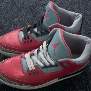 Nike Air Jordans 3 i röd och grå - Säljer ett par Nike Air Jordans i röd och grå färg. Skorna har en cool design med svart och vit snörning och den klassiska Jumpman-loggan på plösen. Perfekta för både vardag och sportiga tillfällen. De har en unik stil med elefantmönster på sulan.