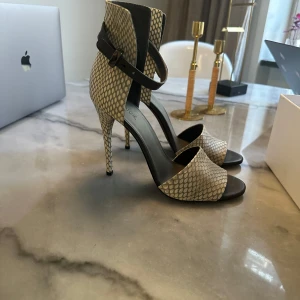 Ormskinnsmönstrade klackskor från Vince - Säljer ett par oanvända sandaletter från Vince i ormskinnsmönster. Skorna har en stilren design med öppen tå och justerbara remmar runt ankeln. Perfekta för en utekväll eller fest! Tillverkade i Italien med högkvalitativt material. 