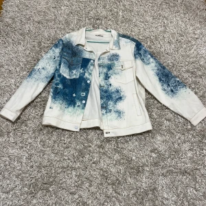  Louis Vuitton Jeans jacka - Säljer en unik vit jeansjacka från Louis Vuitton med blått färgstänk. Jackan har en klassisk krage, knappar framtill och flera fickor. Perfekt för att ge din outfit en cool touch! 💙