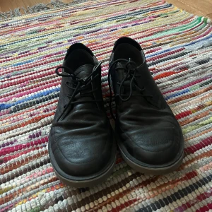 Svarta skinnskor från Camper - Säljer ett par svarta skinnskor från Camper i bra skick. De har en klassisk snörning och en robust sula som ger bra grepp. Perfekta för både vardag och lite finare tillfällen. Skorna är bekväma och stilrena, passar till det mesta i garderoben.