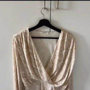 Beige body från NLY One - Säljer en elegant beige omlottklänning från NLY One i storlek S.  Den har ett subtilt mönster och är perfekt för både vardag och fest. 