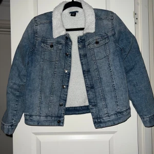 Blå jeansjacka med teddyfoder - Säljer en snygg blå jeansjacka med mysigt vitt teddyfoder. Jackan har långa ärmar och knappar framtill samt på bröstfickorna. Perfekt för höst och vår när du vill hålla dig varm och stilren. Passar till både vardag och fest!
