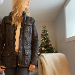 Svart quiltad jacka från Barbour🔛🔝 - Säljer en snygg svart quiltad jacka från Barbour. Den har en klassisk design med guldknappar och dragkedja. Perfekt för höst och vår, och den är i mycket bra skick. Jackan har långa ärmar och en normal passform. Superfin att ha till både vardags och lite finare tillfällen! Pris kan diskuteras men jag kommer ej gå under 200 kr😋
