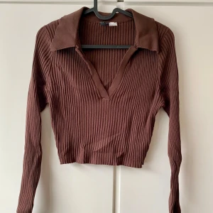 Brun ribbad tröja med krage - Säljer en snygg brun ribbad tröja med krage och v-ringning. Den är croppad och har långa ärmar. Tröjan är i bra skick och passar både till vardags och fest. 