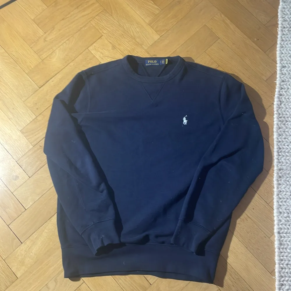 Säljer en stilren svart tröja från Polo Ralph Lauren. Den har en klassisk design med långärmade ärmar och en liten broderad logga på bröstet. Perfekt för både vardag och fest. Passar bra till jeans eller chinos för en avslappnad look. Nypris cirka 2000. Sitter som medium. Den är jämn i färgen det är ljuset som påverkar ifall det ser konstigt ut.. Tröjor & Koftor.