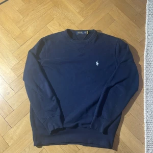 Svart tröja från Polo Ralph Lauren - Säljer en stilren svart tröja från Polo Ralph Lauren. Den har en klassisk design med långärmade ärmar och en liten broderad logga på bröstet. Perfekt för både vardag och fest. Passar bra till jeans eller chinos för en avslappnad look. Nypris cirka 1499. Sitter som medium. Den är jämn i färgen det är ljuset som påverkar ifall det ser konstigt ut.