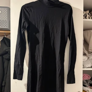 Svart långärmad klänning - Snygg svart långärmad klänning i ett mjukt och stretchigt material. Perfekt för både vardag och festliga tillfällen. Den har en hög krage som ger en elegant touch. Passar bra till höst och vinter.