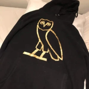 Svart hoodie från October's Very Own - Säljer en svart hoodie från October's Very Own i storlek L. Skickas med äkthetsbevis! Den har en stor, guldig uggla på framsidan som ger en cool och unik look. Perfekt för höst och vinter med sin mysiga passform och känguruficka framtill. Made in Canada, så kvaliteten är på topp! 🦉✨