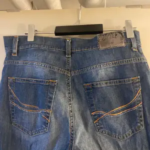 Säljer ett par klassiska blå jeans i storlek 38. De har en snygg straight passform och är tillverkade i bomull med lite elastan för extra komfort. Jeansen har dekorativa sömmar på bakfickorna och en traditionell femficksdesign. Perfekta för vardagsbruk!