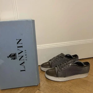 Grå sneakers från Lanvin - Säljer ett par stilrena grå sneakers från Lanvin i mycket bra skick. Skorna har en snygg kombination av grått tyg och mörkare grått skinn på tån och hälen. De har en vit sula och klassisk snörning. Perfekta för både vardag och fest! Kan sänka pris i ytterst snabb affär