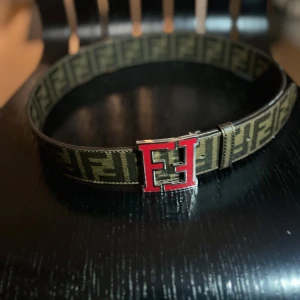 Brunt bälte från Fendi - Säljer ett snyggt brunt bälte från Fendi med det ikoniska FF-mönstret. Bältet är 95 cm långt och har ett coolt spänne i rött och silver. Perfekt för att ge din outfit en lyxig touch. Använd det till både vardag och fest!