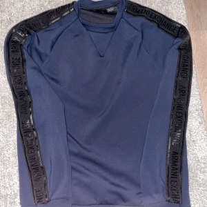 Tröja från Armani Exchange - Säljer en snygg mörkblå tröja från Armani Exchange. Den har långa ärmar med svarta detaljer och text längs ärmarna. Perfekt för en stilren och modern look. Passar bra till både vardag och fest. Skriv vid minsta lilla fundering✍️😀✅