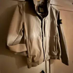 Säljer en snygg beige jacka från Stone Island i storlek S. Jackan har en dragkedja framtill och en ikonisk logga på ärmen. Perfekt för höst och vår, med en stilren design som passar till det mesta. Jackan är i mycket bra skick och redo för nya äventyr!