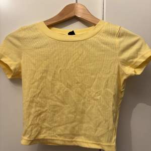 Säljer en söt gul ribbad t-shirt i mycket bra skick. Den har en tight passform och korta ärmar, perfekt för sommardagar. Materialet är mjukt och stretchigt, vilket gör den superbekväm att bära 🌼