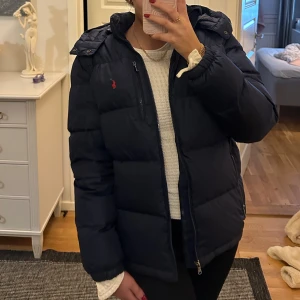 Mörkblå dunjacka från Ralph Lauren - Säljer en snygg och varm mörkblå dunjacka från Ralph Lauren. Jackan har en dragkedja framtill och en liten röd logga på bröstet. Perfekt för kalla vinterdagar! Jackan är i storlek 18-20 år vilket är en XL i kidsstorlek men sitter som en S/XS i vuxenstorlek. Passar både för tjejer och killar. Den är i mycket bra skick. Köptes för 3000 kr men säljer för 1500 kr🩷