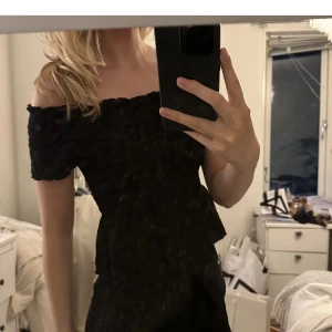 Svart offshoulder klänning - Säljer en elegant svart offshoulder topp i mycket bra skick. Perfekt för festliga tillfällen med sin stilrena design. Toppen har en tight passform som framhäver figuren och är tillverkad i ett bekvämt material.