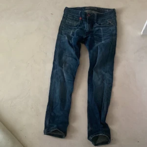 Blå jeans från Replay - Snygga blå jeans från Replay med klassisk femficksdesign och knappgylf. De har en mörk tvätt med lätt slitna detaljer för en cool look. Perfekta för en avslappnad stil och grisch stil. Str 29-32