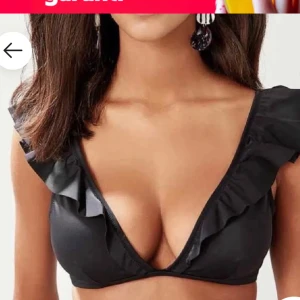 Svart bikiniöverdel med volangdetaljer - Snygg svart bikiniöverdel med volangdetaljer längs axelbanden och en djup v-ringning. Helt ny,oanvänd!