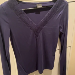 Mörkblå långärmad topp med spetsdetaljer - Snygg mörkblå topp från ginatricot med långa ärmar och v-ringning dekorerad med spets. Perfekt för en stilren look. Helt osnvänd