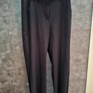 Svarta kostymbyxor - Eleganta svarta kostymbyxor med en klassisk design. De har en rak passform och är perfekta för en stilren look. Byxorna har fickor fram och en diskret "fejk" ficka bak. Aldrig använda 