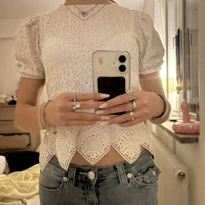 Vit spetsblus - Charmig vit blus med korta ärmar och spetsdetaljer. Den har en vacker struktur och en unik kantdesign som ger en romantisk känsla. Perfekt för att lyfta vilken outfit som helst.