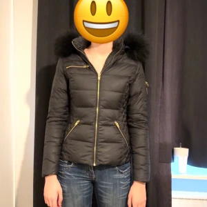 Svart päls jacka från Rockandblue - Snygg svart dunjacka från Rockandblue med pälskantad huva av tvättbjörn och guldfärgade dragkedjor. Jackan har en quiltad design och sex fickor (två på insidan). Storlek 34. För fler bilder kom privat. Original pris är runt 3000kr