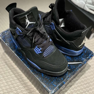 Svarta och blå jordan 4 Thunder blue  - Snygga svarta Nike Air Jordans med blå detaljer och klassisk Jumpman-logga. Skorna har snörning och en stilren design som passar perfekt för sneakerheads. Bra sick 