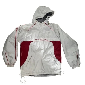 Vintage umbro windbreaker  - Säljer en vit och röd vindjacka från Umbro med huva och dragkedja. Jackan har långa ärmar och elastiska muddar. Perfekt för blåsiga dagar med sin sportiga look och praktiska fickor.