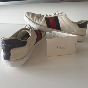Vita sneakers från Gucci - Snygga vita sneakers från Gucci med klassiska ränder i rött och blått på sidan. Skorna har snörning och en bekväm passform. Perfekta för en stilren look. Priset kan diskuteras!