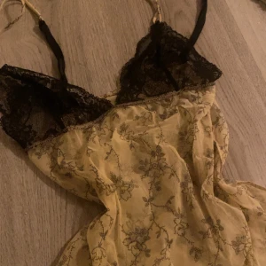 Topp med spets  - svarta spetsdetaljer och blommigt mönster, tunna axelband och en elegant design som ger en romantisk känsla. 