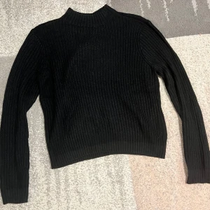 Svart ribbad tröja - Säljer en stilren svart ribbad tröja med långa ärmar. Perfekt för kyligare dagar och lätt att matcha med olika outfits. Tröjan har en klassisk design med en bekväm passform.